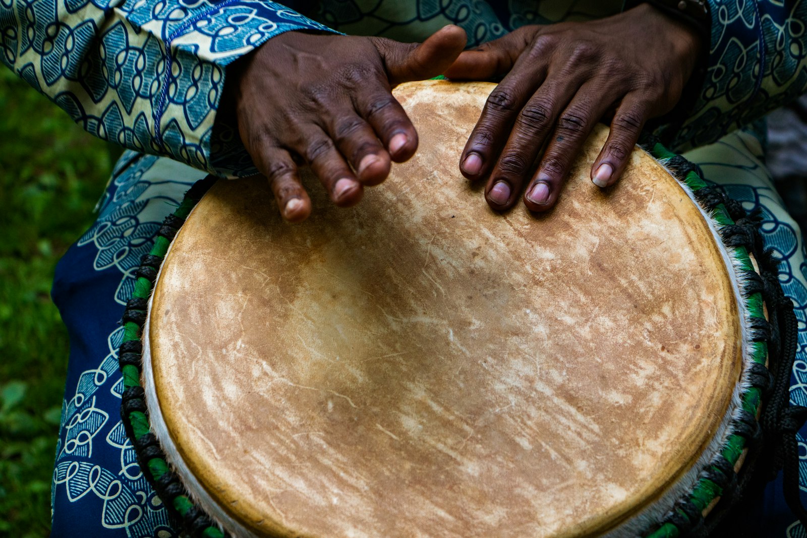 Close view of two hands resting on the skin of a hand drum, the kind of percussion that carries the groove rather than the kick