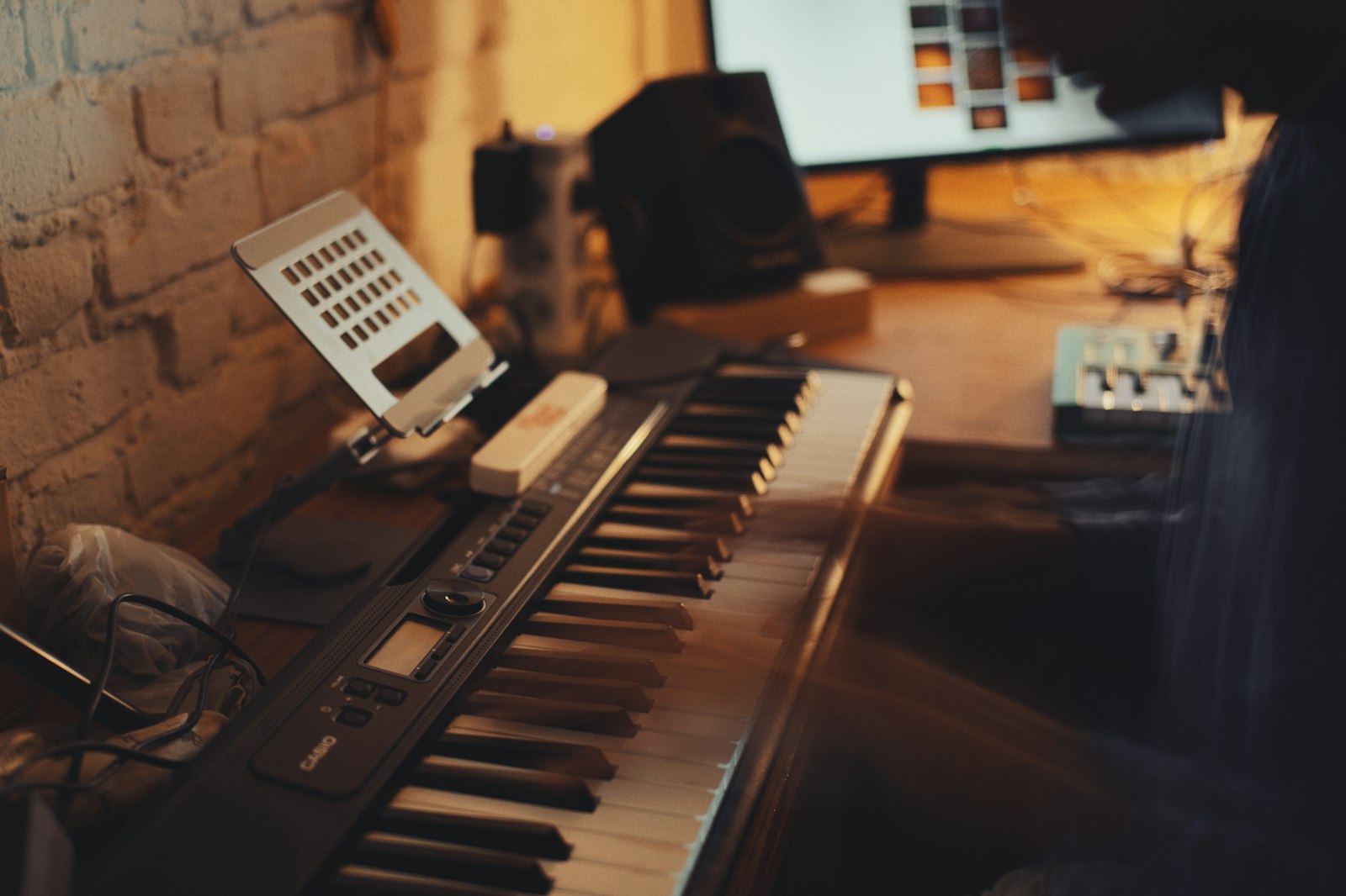 A keyboard and a monitor speaker in a dimly lit home studio, the kind of setup an ambient track with no drums gets written on