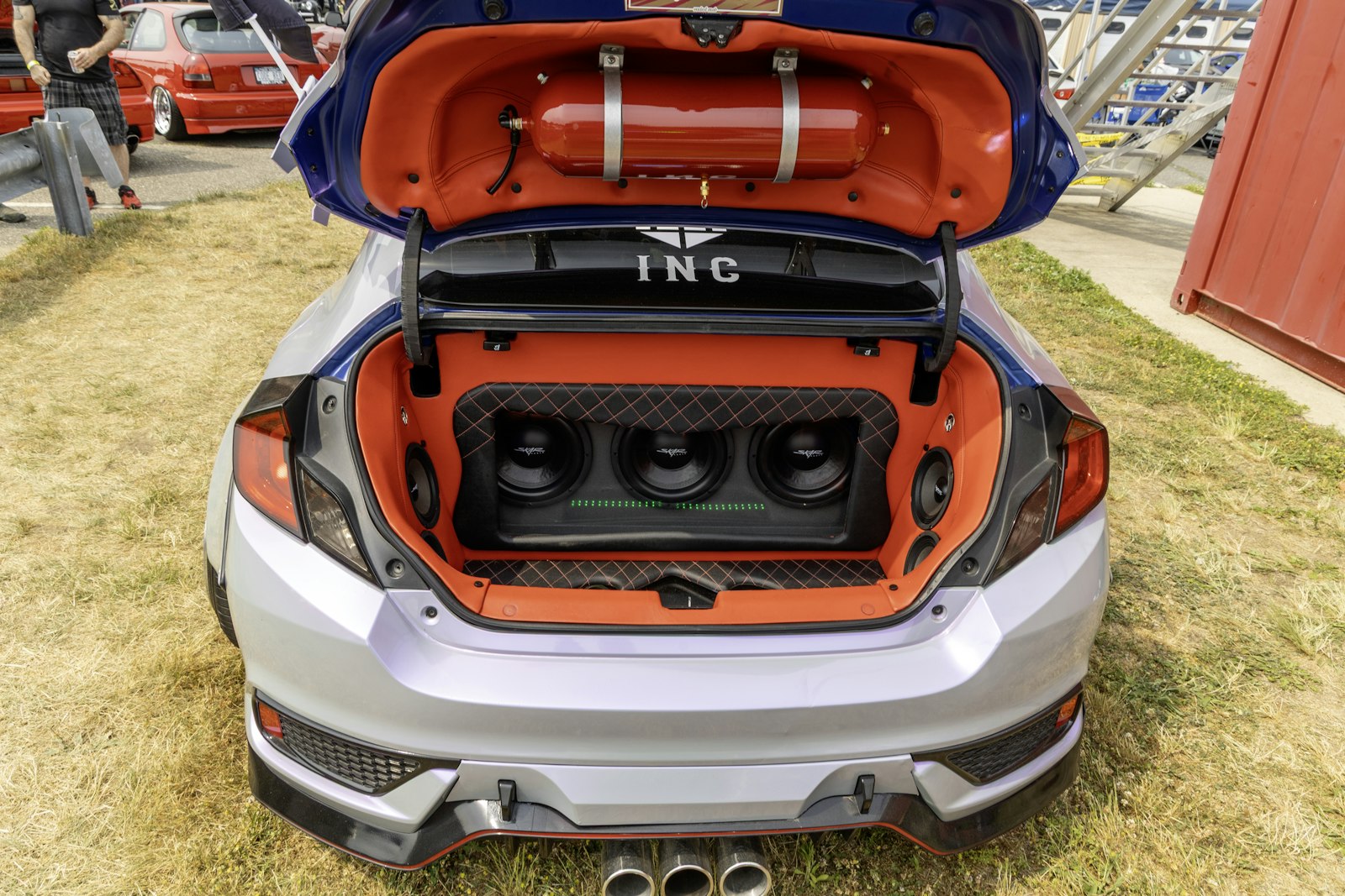 An open car boot at a show with three subwoofers mounted in a custom orange trimmed enclosure, the kind of install a bass boosted edit is made for