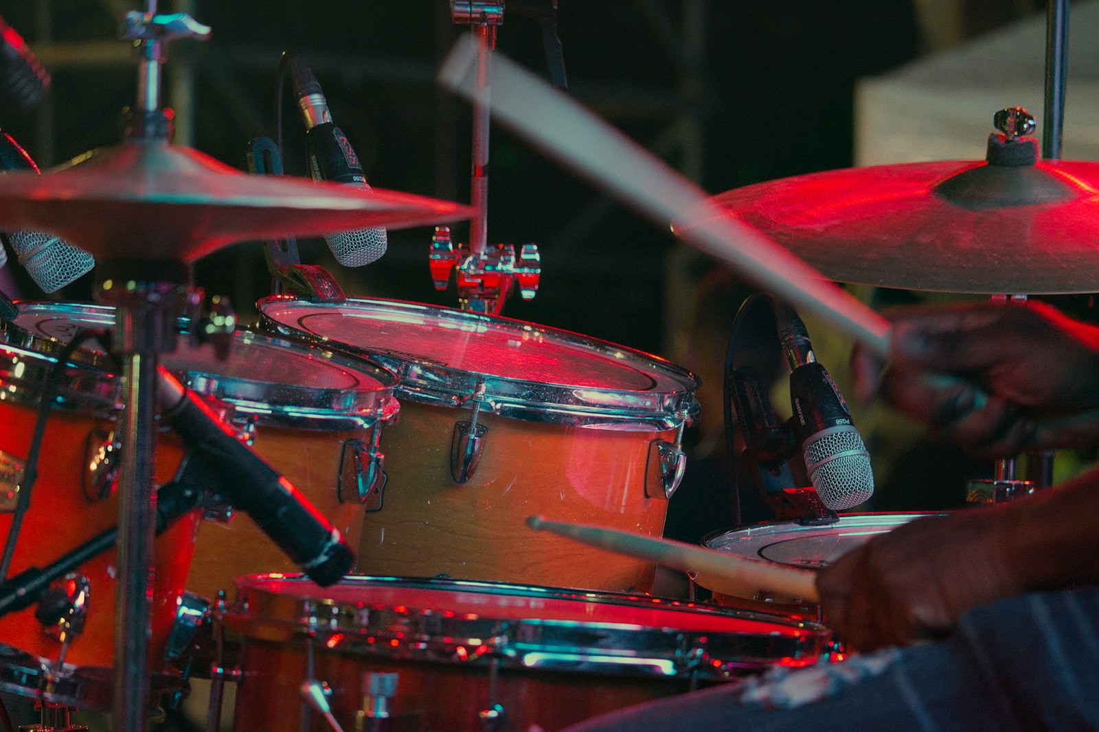 A close up of a mic'd drum kit under red stage light with the sticks blurred mid stroke