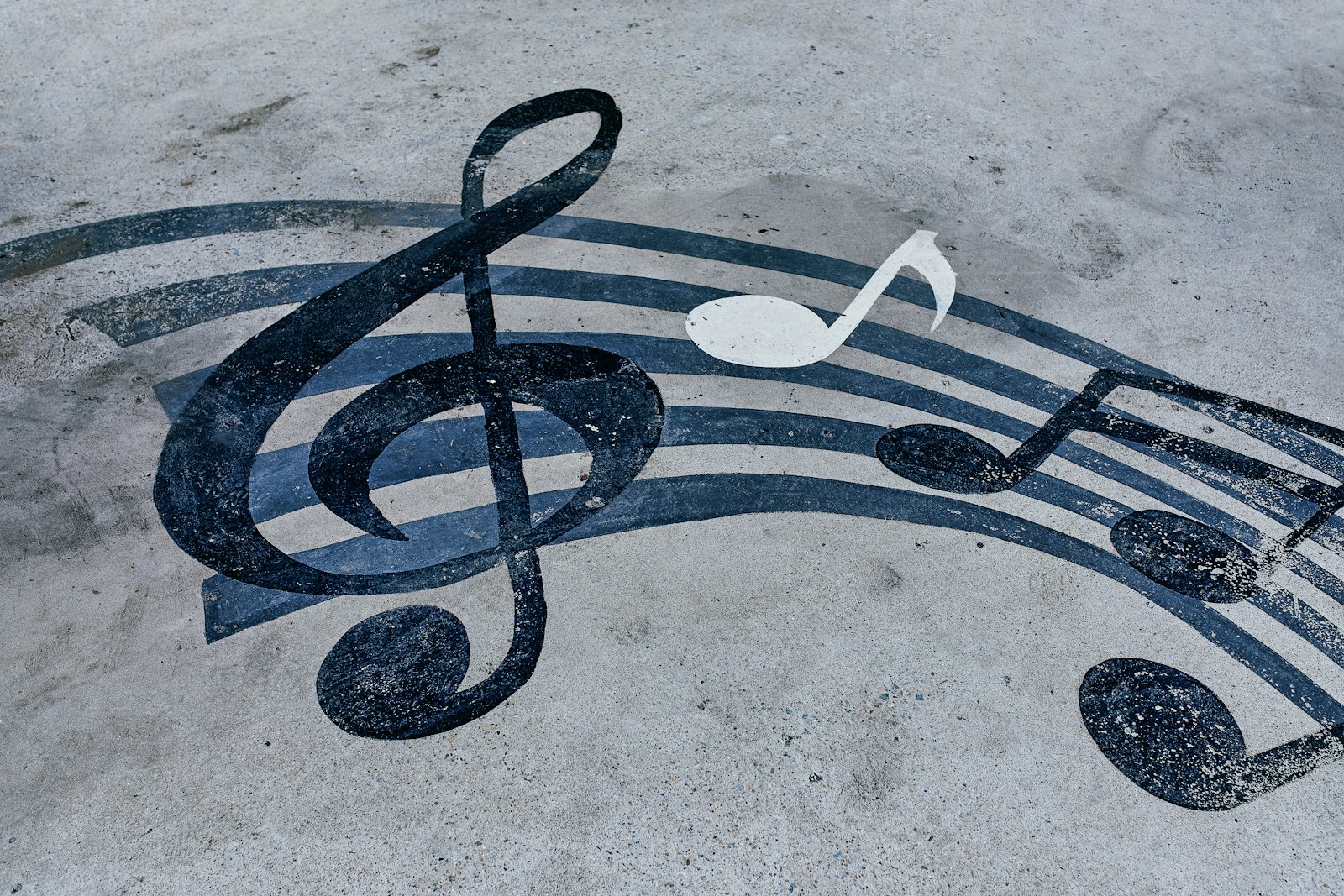 Large music notes and a treble clef painted across grey concrete, one eighth note picked out in white while the rest are dark blue