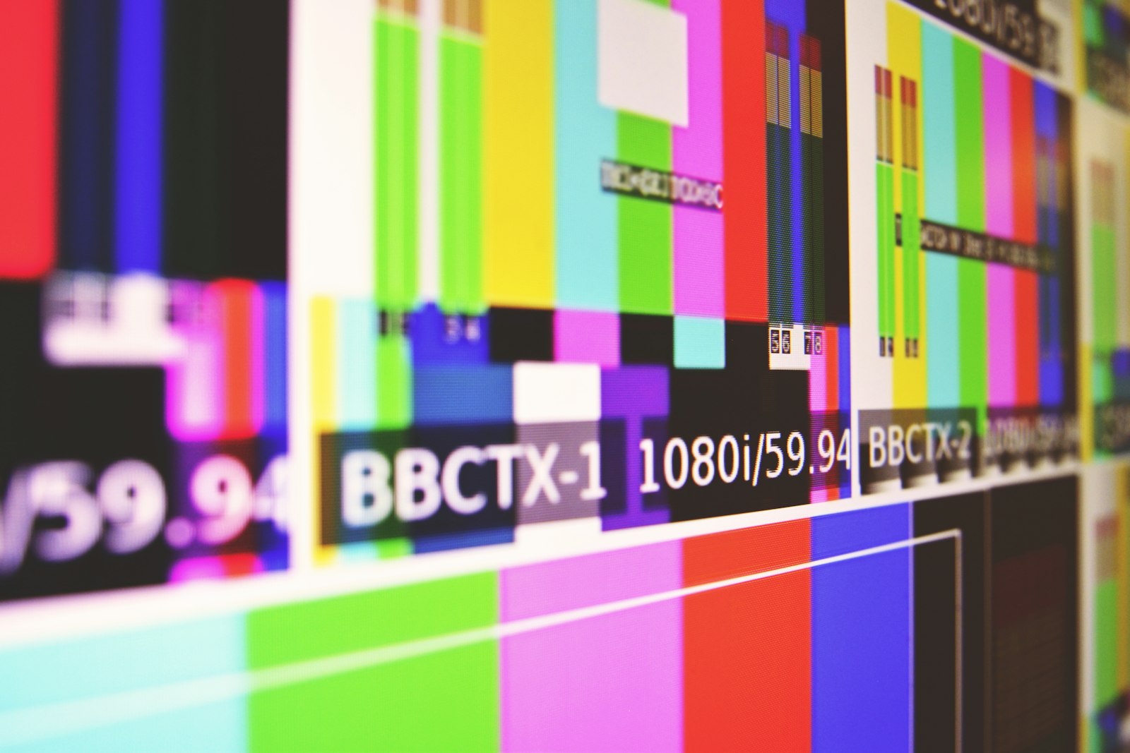 A wall of broadcast monitors showing colour bar test patterns with 1080i/59.94 signal labels across them, the reference picture an engineer checks a video feed against