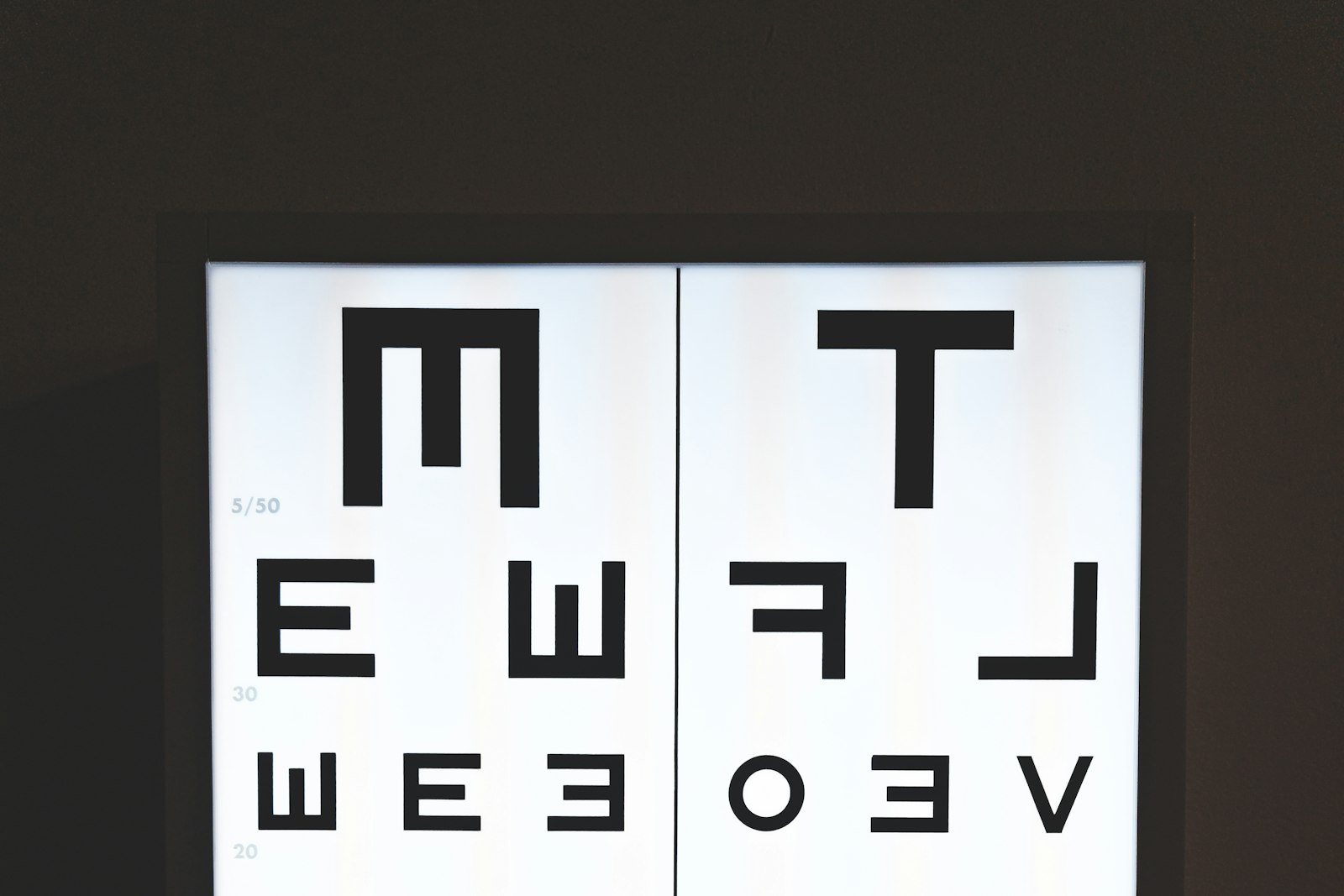 A backlit optician's eye chart on a dark wall, its mirrored letters shrinking row by row down the panel past the 30 and 20 line markers